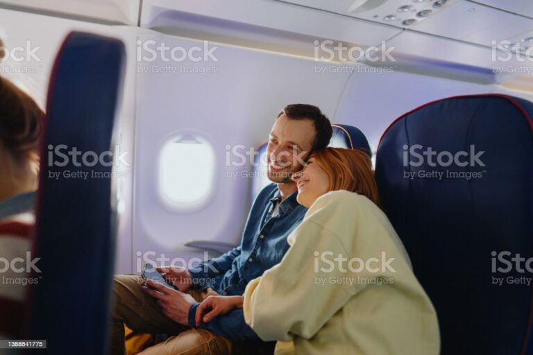 Photo of a newlywed couple traveling by plane; enjoying their flight and being excited about their belated honeymoon trip due to a disease outbreak.