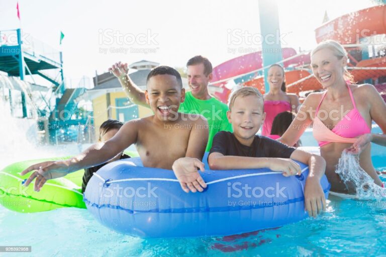 A multi-ethnic group of family and friends having fun on the lazy river at a water park. Two boys in front are sharing an inflatable innertube.